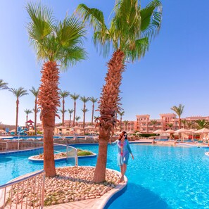 A pool area with palm trees, a clear blue sky, and a building in the background. - Beach Albatros Resort - All Inclusive  (Hurghada)