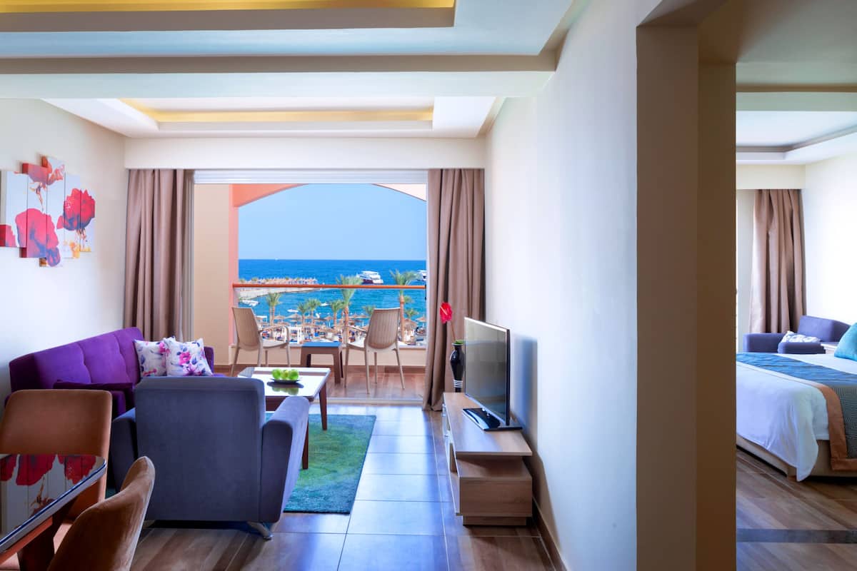 Une chambre d’hôtel avec un balcon donnant sur une plage, un canapé, une télévision et un coin repas avec vue sur la mer.