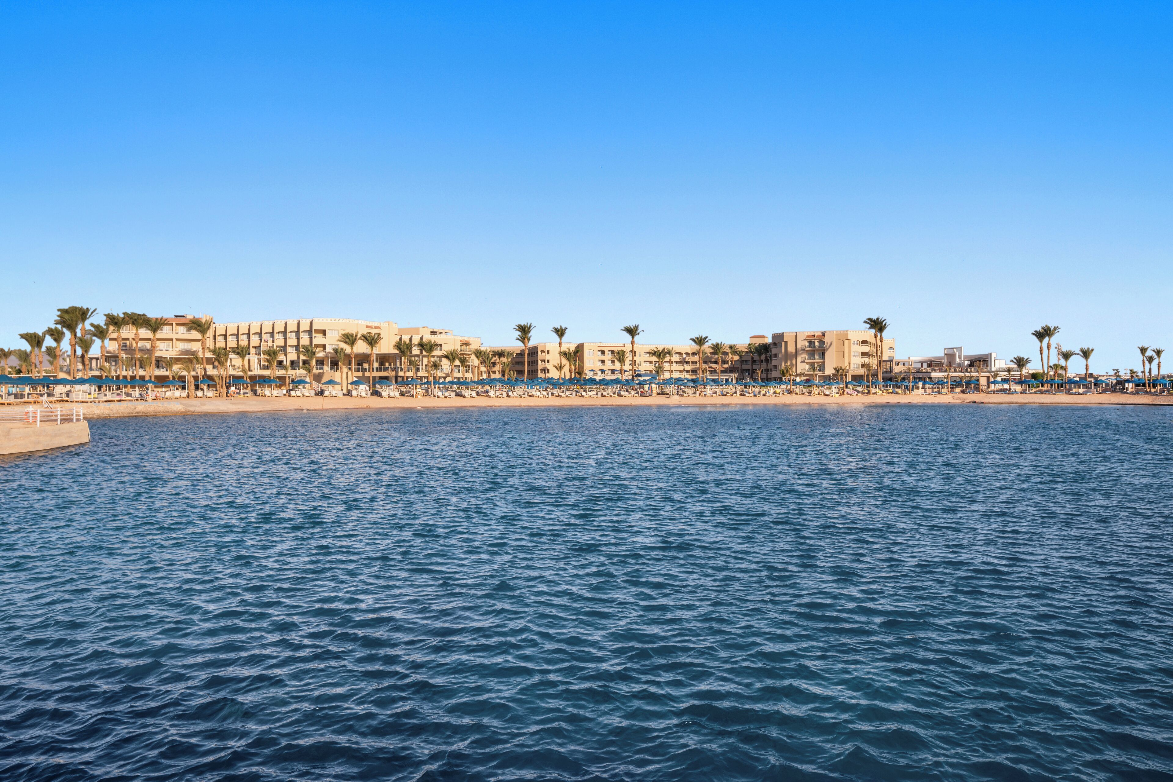 Un hotel frente al mar con vista a la playa, varios pisos y palmeras.