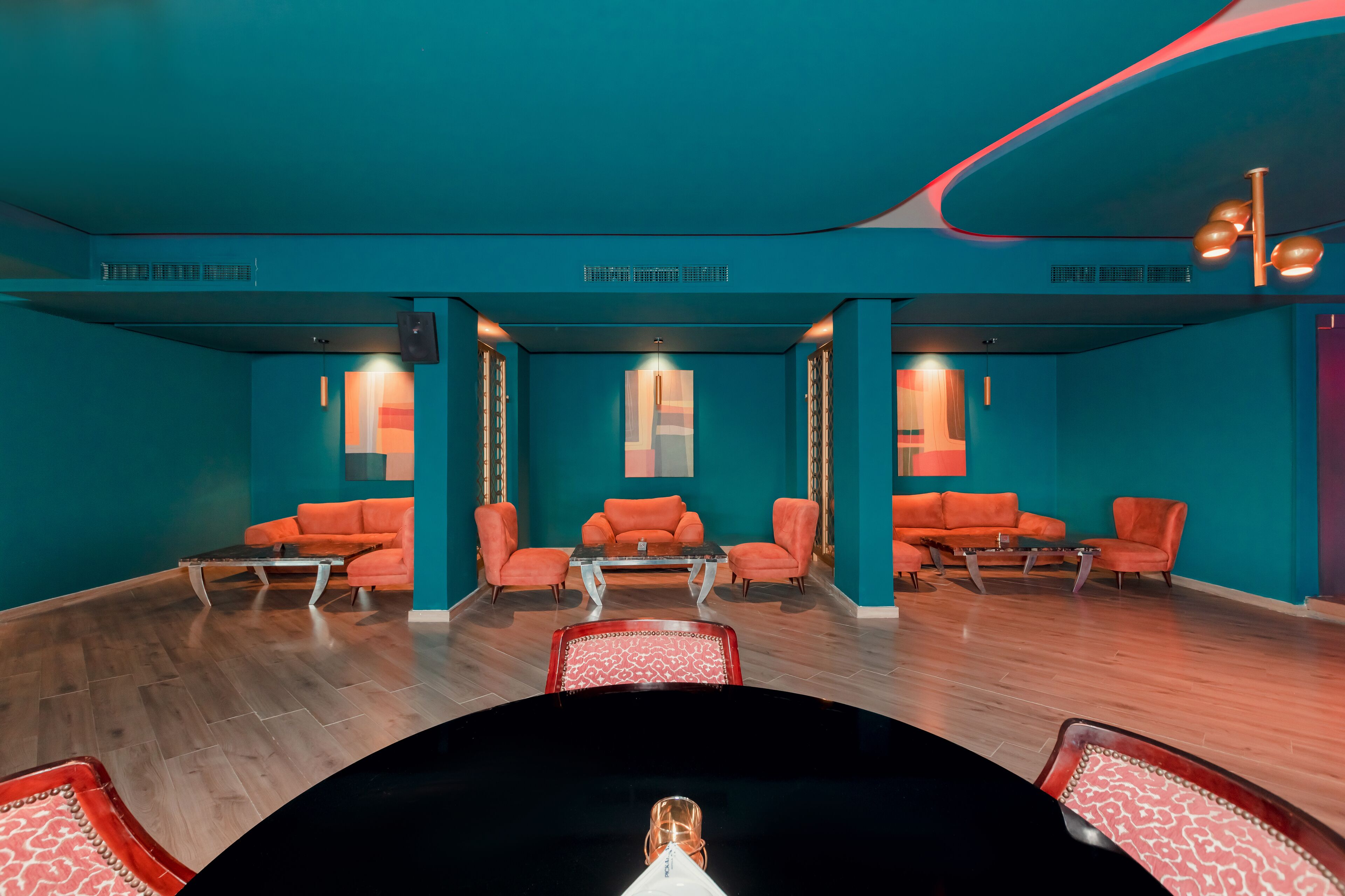 Une pièce aux murs de couleur turquoise, meublée de meubles orange, avec une table centrale et une table ronde noire au premier plan.