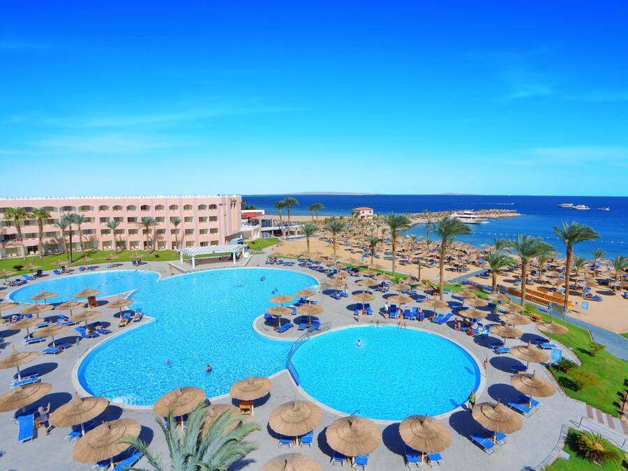 Ett semesterhotell med två stora pooler, parasoller och utsikt över havet.