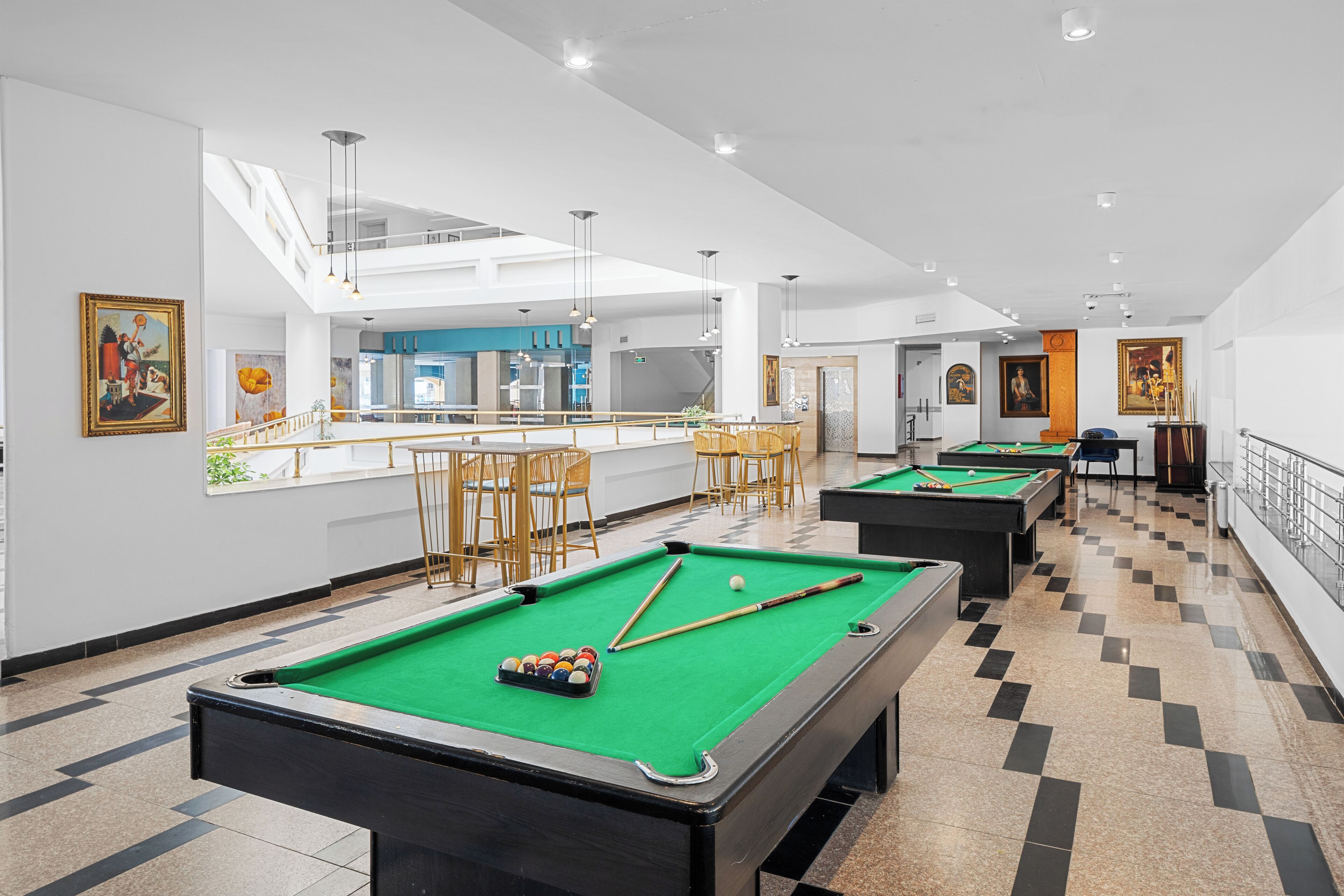 A pool area with multiple tables and chairs, a bar, and artwork on the walls.