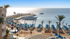 A beach resort with a large white yacht docked near the shore, numerous blue umbrellas, and palm trees. - Beach Albatros Resort - All Inclusive  (Hurghada)