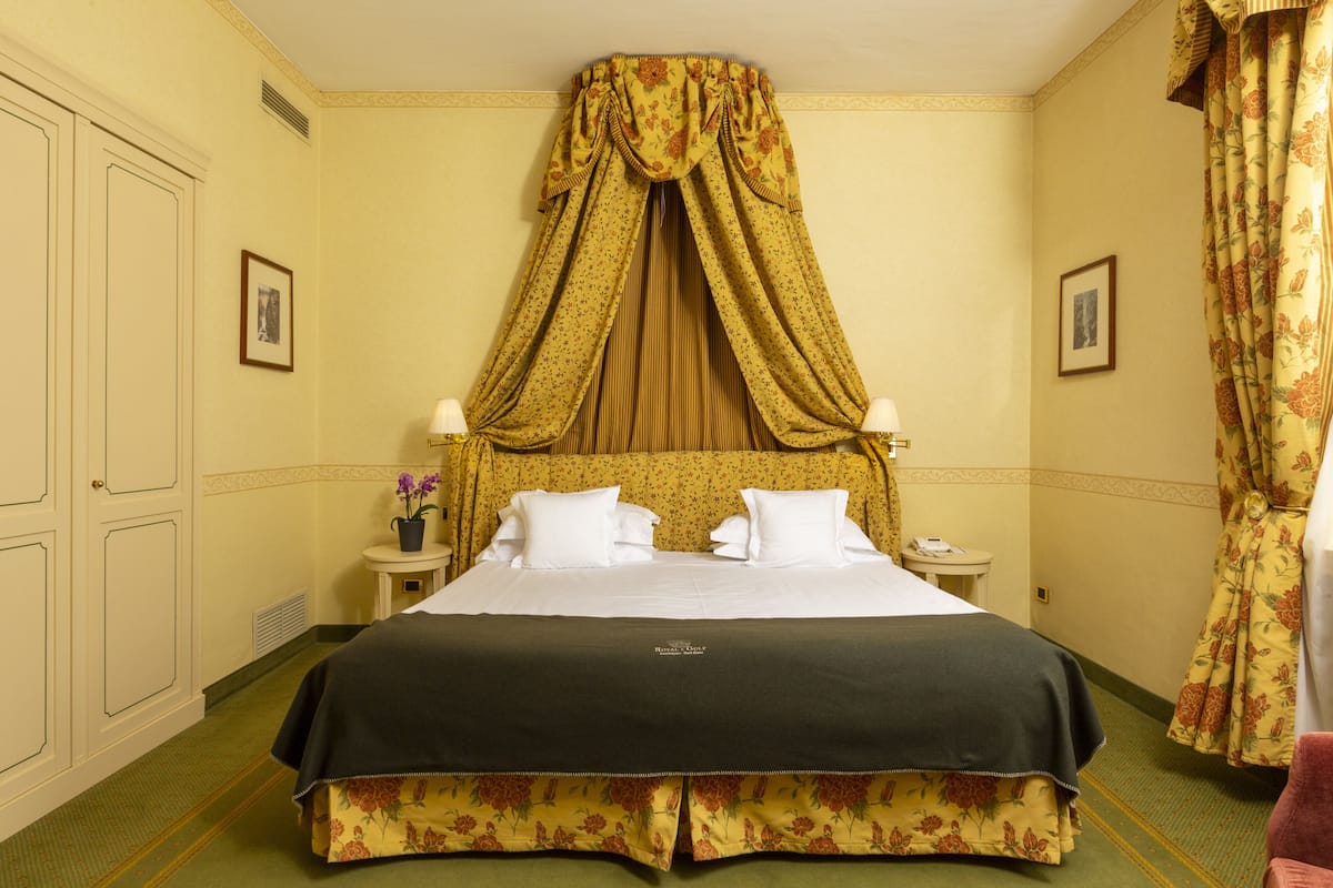 A hotel room with a large bed, a canopy, two bedside tables with lamps, and floral curtains.