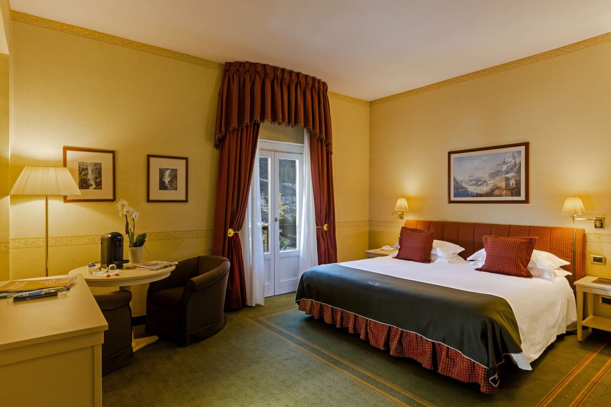 A hotel room with a bed, desk, chair, and a door with curtains.