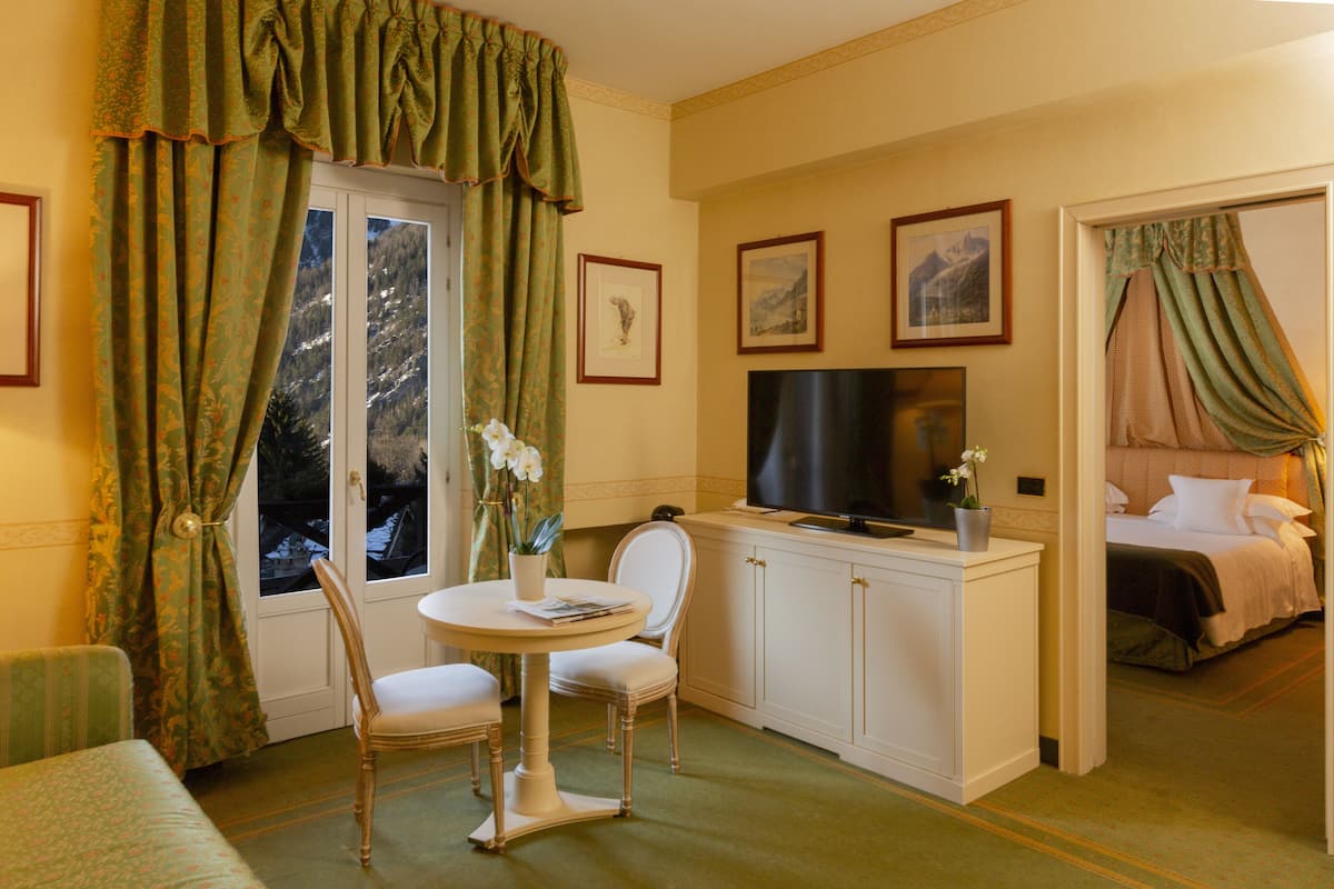 A hotel room with a television, a bed, a dining area with a table and chairs, and a window with curtains.