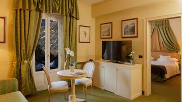 Ein Hotelzimmer mit Fernseher, einem Bett, einer Essecke mit Tisch und Stühlen sowie einem Fenster mit Vorhängen.