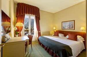 Habitación de hotel con una cama, dos lámparas de noche, un escritorio con lámpara, una silla y una ventana con cortinas.