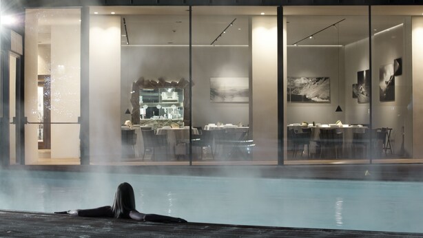 A modern indoor pool area with a glass wall separating the pool from a dining area.