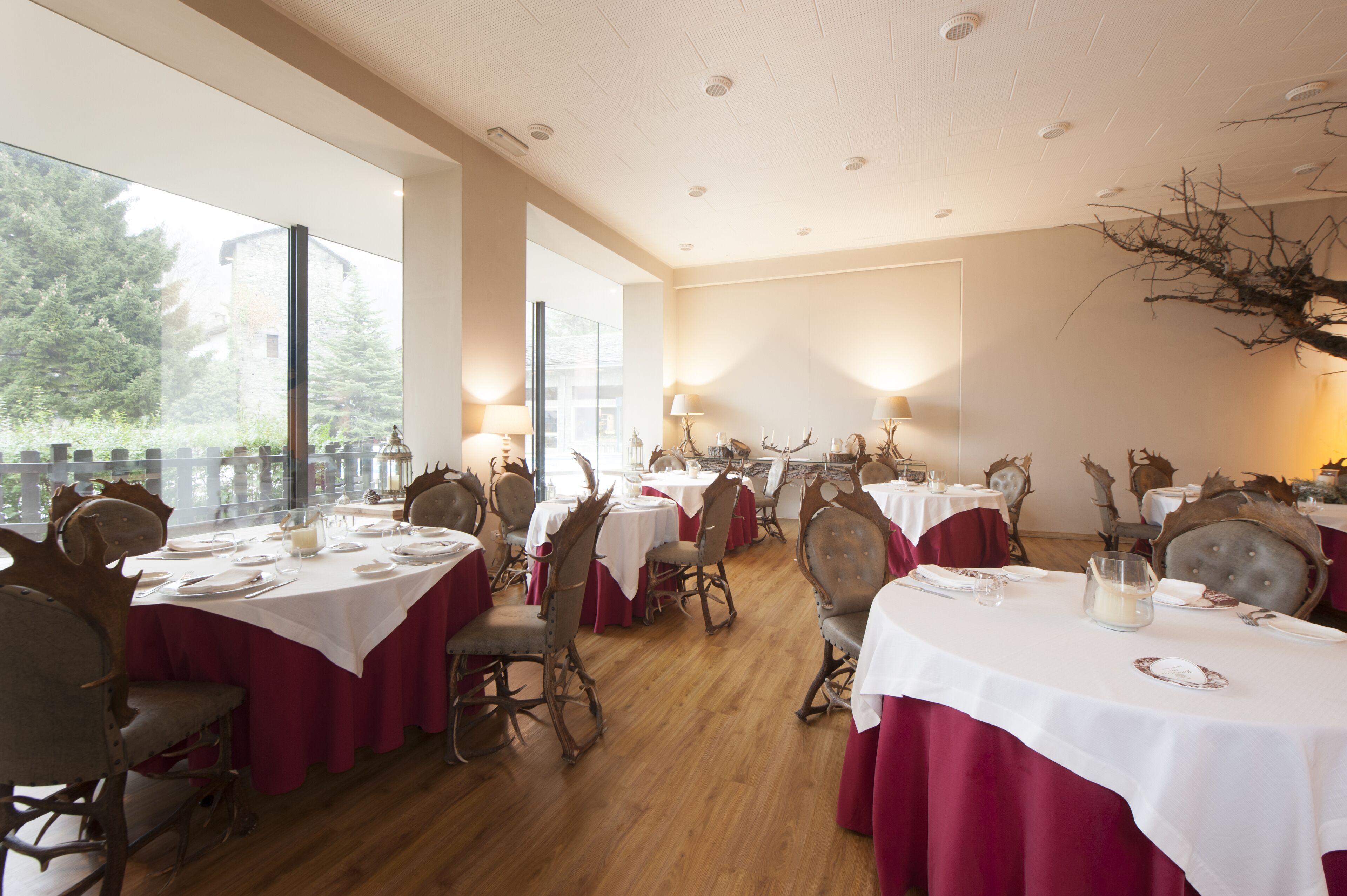A dining area with tables set for multiple guests, featuring classic chairs and a view of the outdoors through large windows.