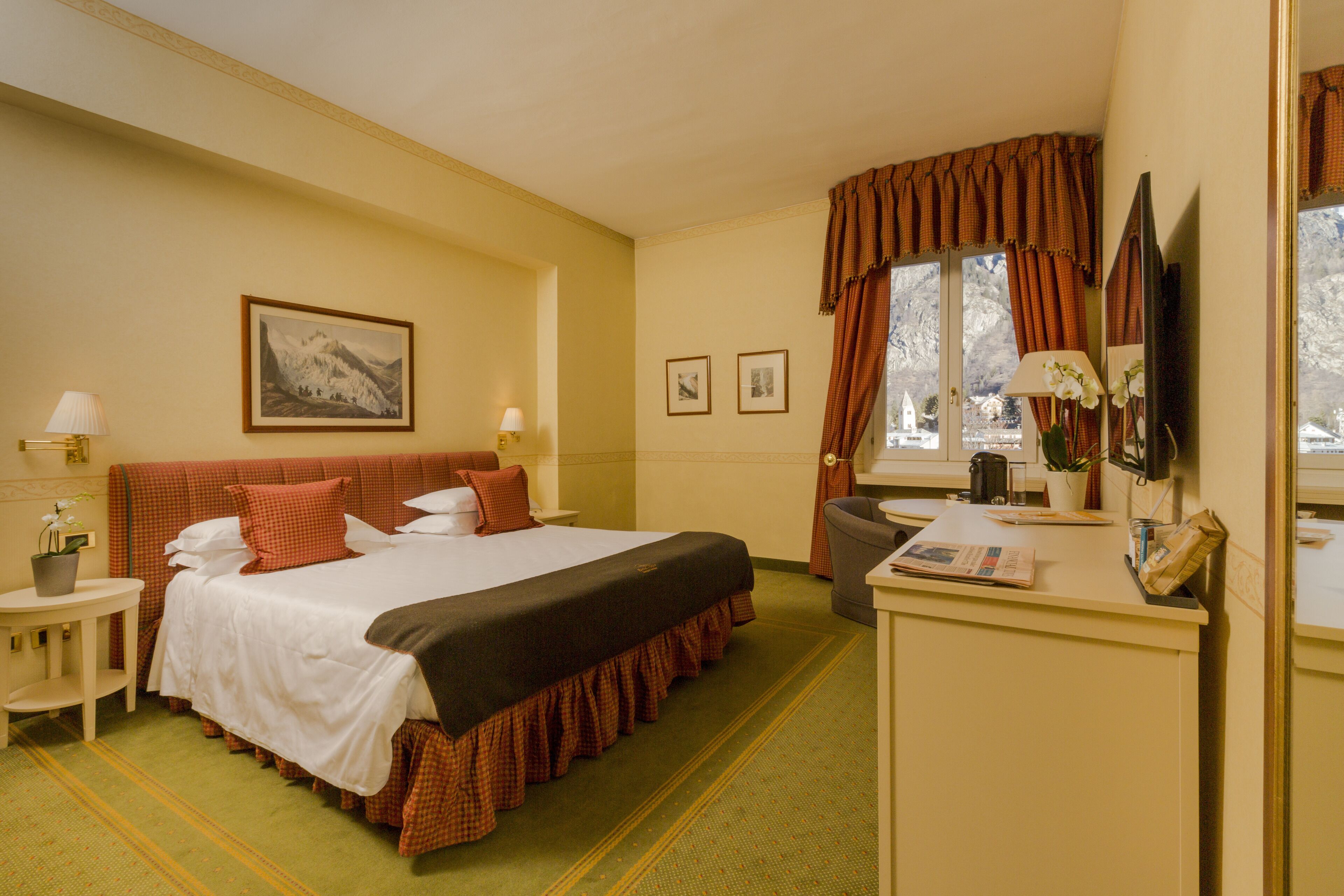 Ein Hotelzimmer mit einem großen Bett, einem Schreibtisch mit Stuhl, einem Fernseher und einem Fenster mit Vorhängen.