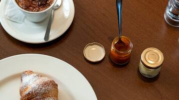 A table with a croissant, a chocolate dessert, a spoon, a jar of jam, and a menu.