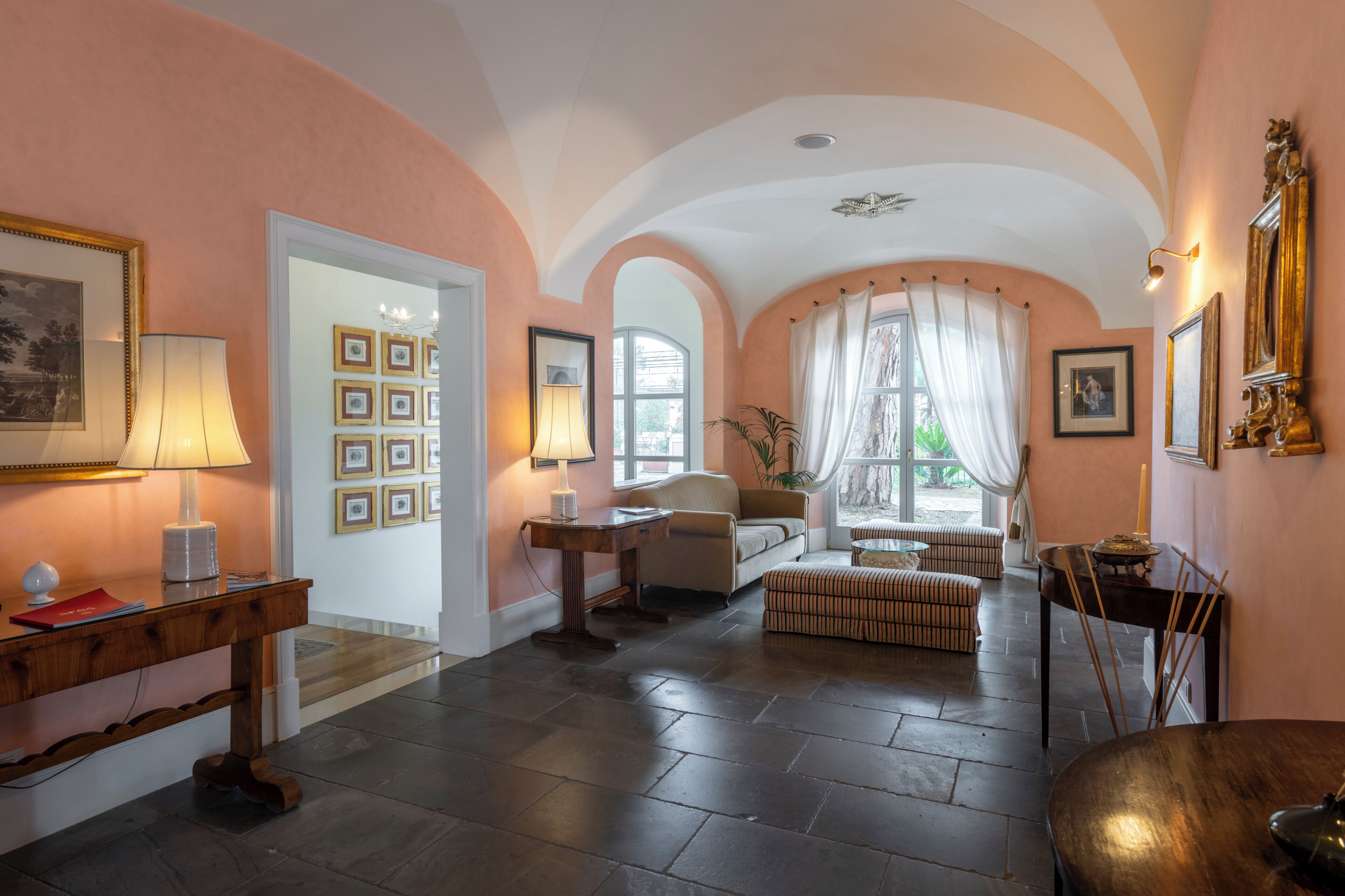 Een ruime kamer met een hoge plafond, een bank, een tafel en een raam met gordijnen.