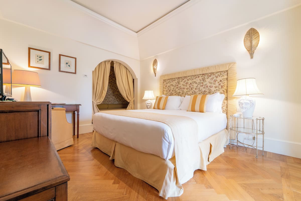 A hotel room with a large bed, a desk, a chair, a lamp, and a decorative wall piece.