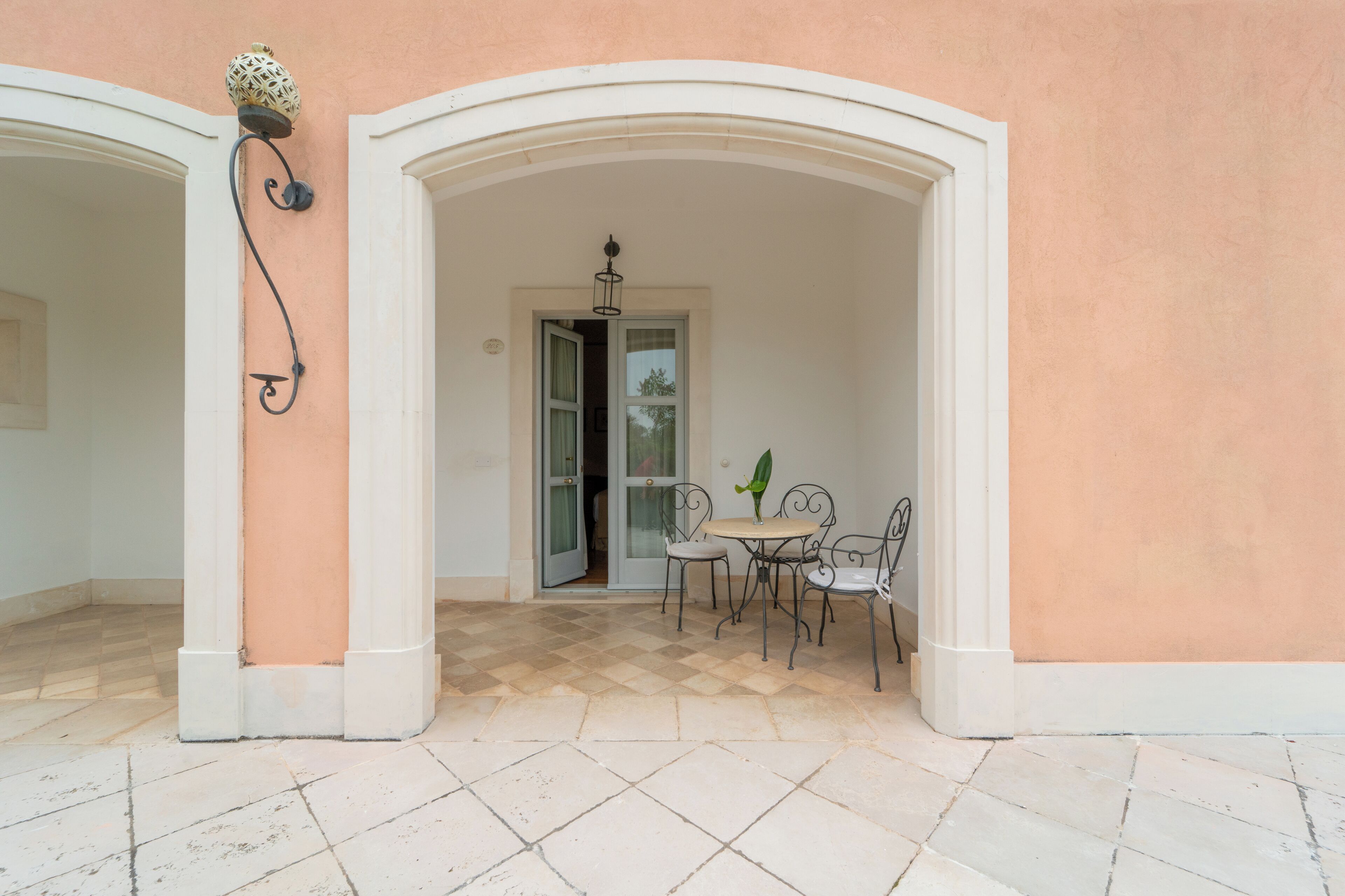 Un patio al aire libre con piso a cuadros, una mesa con sillas y una puerta que da a un espacio interior.