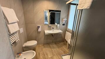 A modern bathroom with a toilet, bidet, sink, and glass shower enclosure.