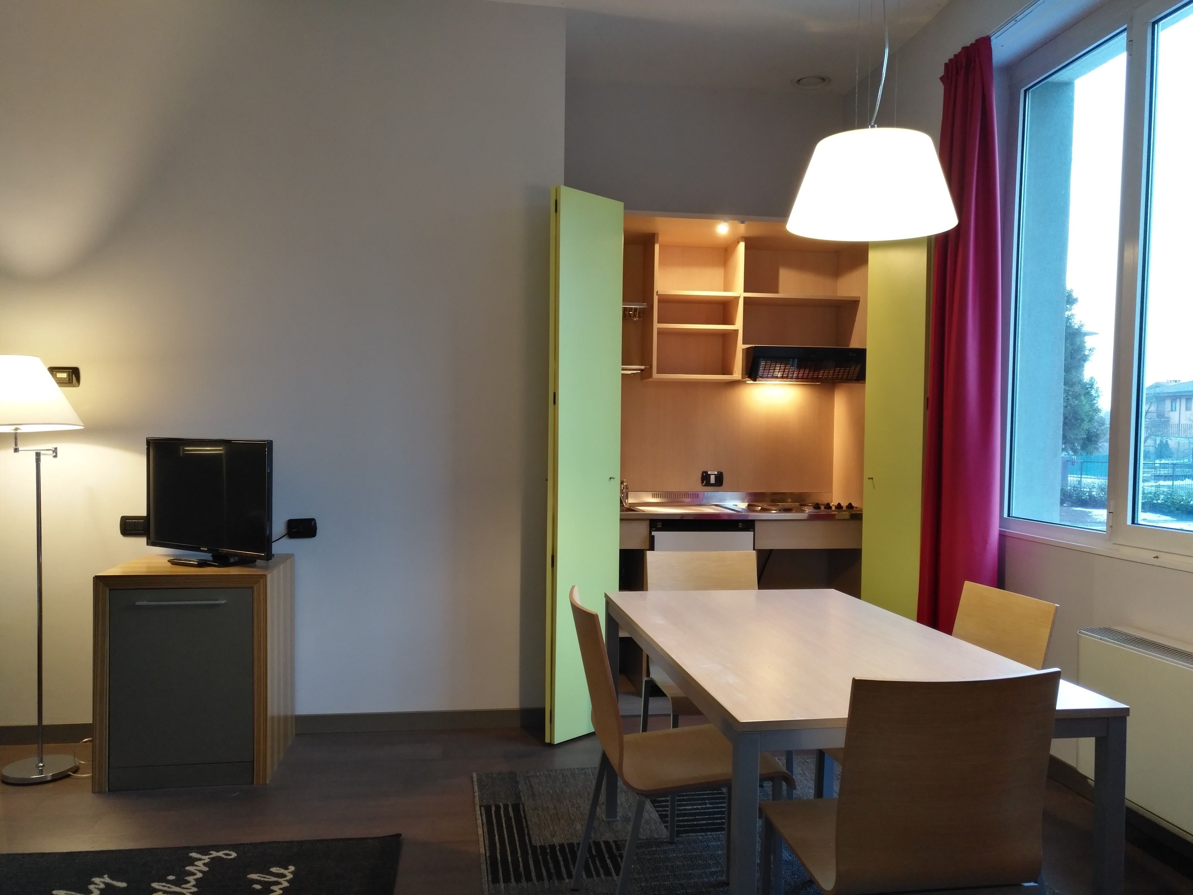 A compact room with a TV, a dining table, and a kitchenette.