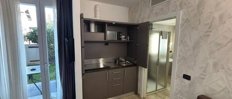 Eine kompakte Küche mit einer Schiebetür, die auf einen Balkon führt, einer eingebauten Mikrowelle und einer kleinen Arbeitsfläche.