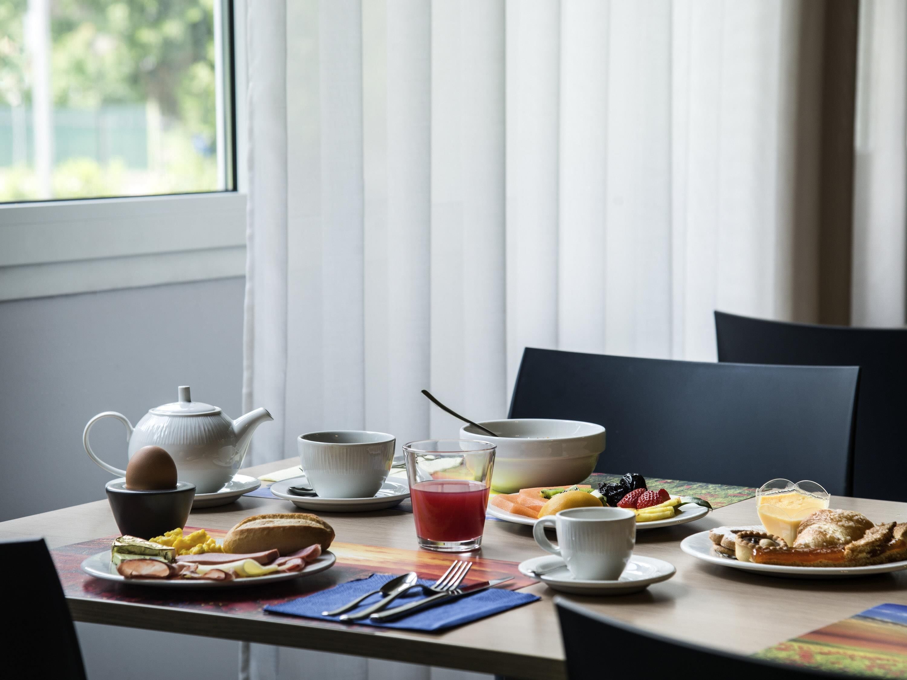 Aamiaispöytä, jolla on teekannu, kuppeja, lautasellisia ruokaa ja hedelmäkulho.