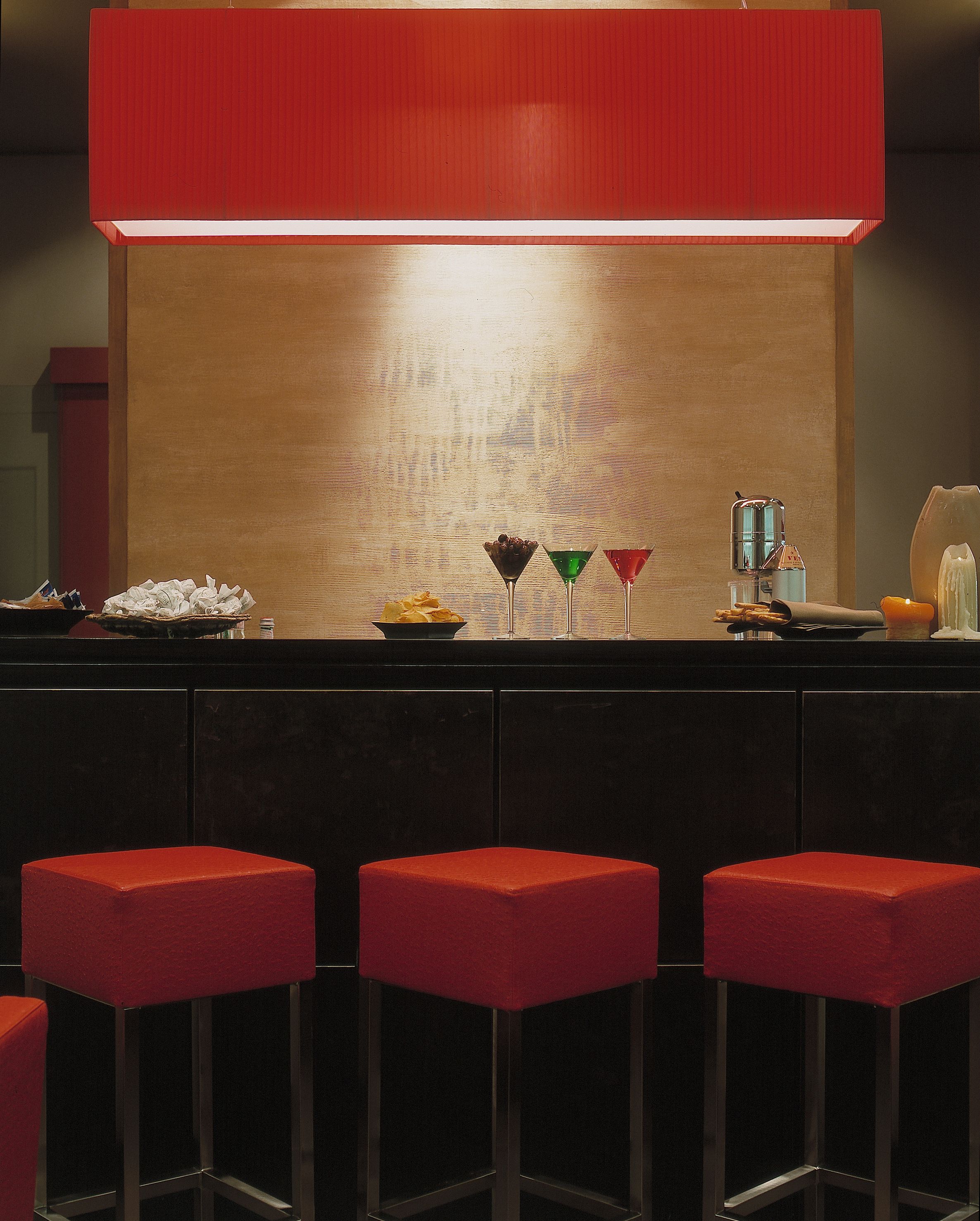 A bar area with a red bar counter, stools, and a variety of drinks and snacks.