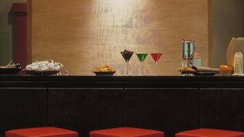 A bar area with a red bar counter, stools, and a variety of drinks and snacks.