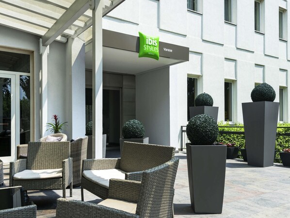 A hotel exterior with wicker furniture, potted plants, and a sign for ibis Styles Hotels. - Bis Hotel Varese (Varese)