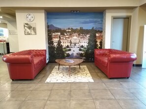 Un vestíbulo con dos sofás de cuero rojo, una mesa de centro de madera, un reloj y un mural de un paisaje urbano.