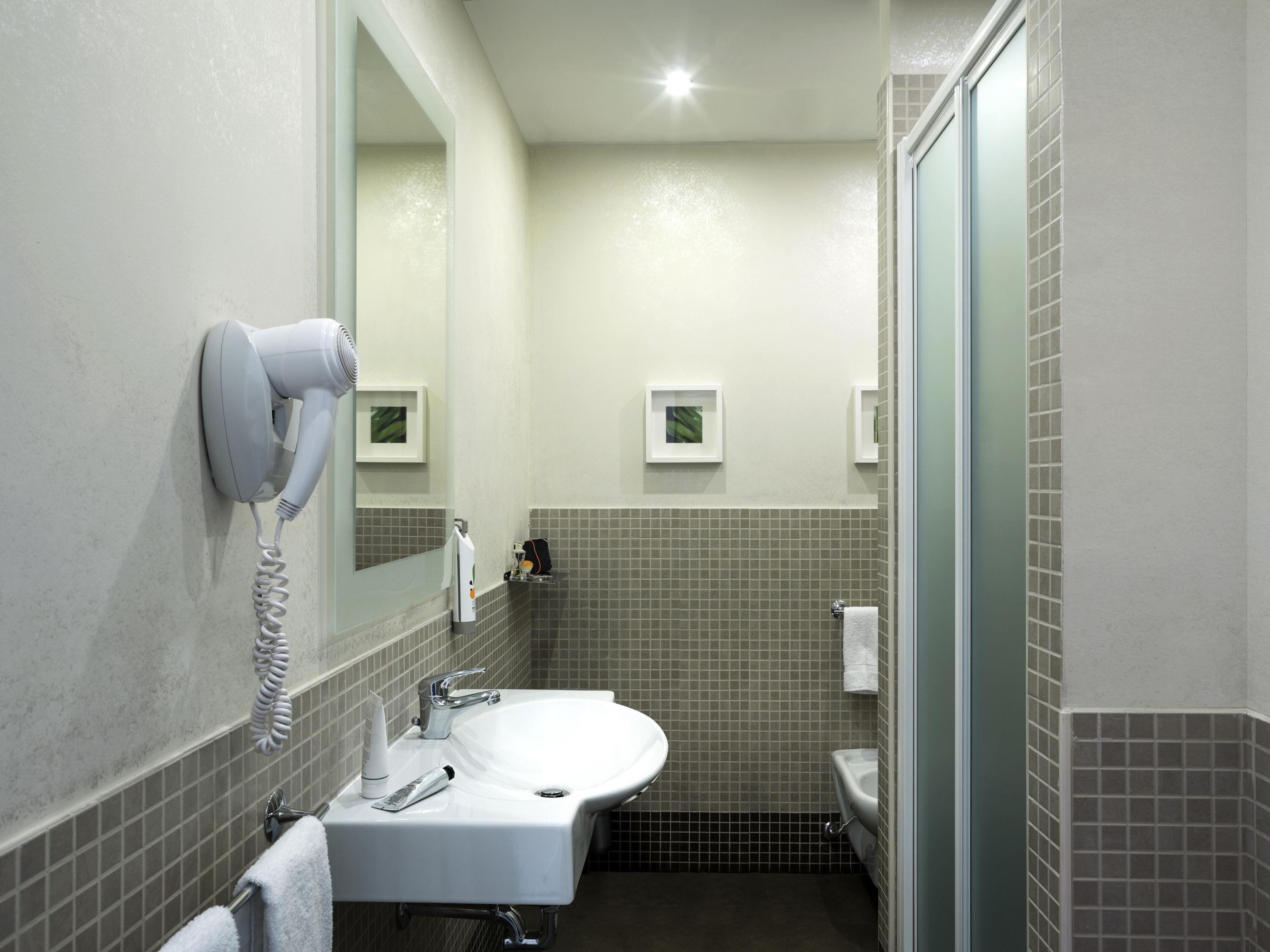 A bathroom with a white sink, a hairdryer mounted on the wall, and a mirror above the sink.