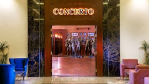 A hotel lobby with a marble reception desk, a 'CONCERTO' sign, and a statue of musicians.
