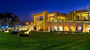 A large, well-lit building with a prominent entrance and multiple levels, surrounded by a well-maintained lawn and palm trees.