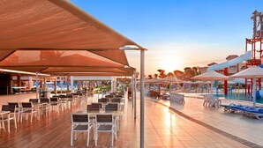 A covered outdoor seating area with tables and chairs, a poolside area with umbrellas, and a water slide.