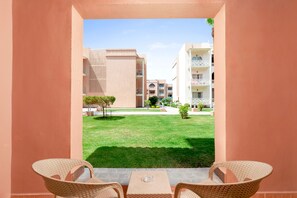 Un espace extérieur aménagé avec des chaises et une table en osier, offrant une vue sur une pelouse bien entretenue et des bâtiments en arrière-plan.
