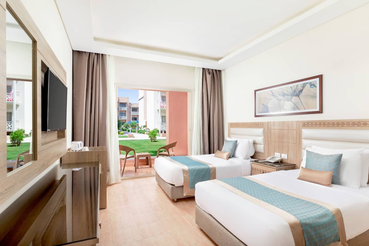A hotel room with two beds, a TV, a desk, and a view of the outside.