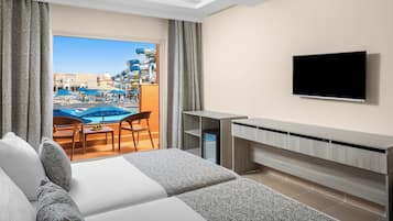 A hotel room with a bed, a desk, a TV, and a view of a pool and outdoor area.