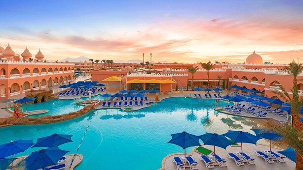 A resort pool area with multiple sun loungers and umbrellas, surrounded by a building with arches and domes.