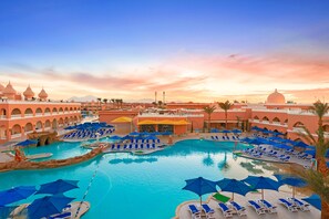 A resort pool area with multiple sun loungers and umbrellas, surrounded by a building with arches and domes. - Pickalbatros Alf Leila Wa Leila Resort - Neverland Hurghada (Hurghada)