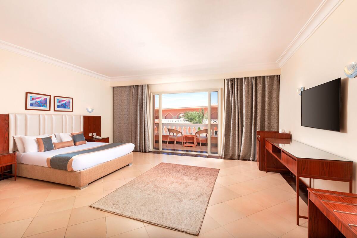 Een hotelkamer met een bed, bureau, televisie en een balkon met een tafel en stoelen.
