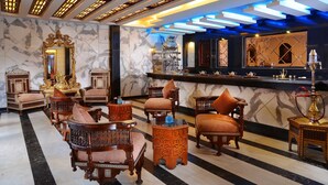 Un vestíbulo lujoso con muebles de madera ornamentados, paredes de mármol y una zona de bar con una lámpara moderna.