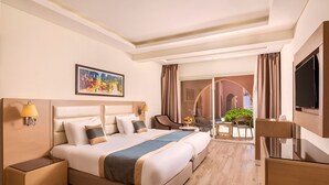 A hotel room with a large bed, a desk, a chair, a TV, and a painting on the wall.