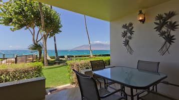 A patio with a glass table and chairs, a view of the ocean, and decorative wall art.