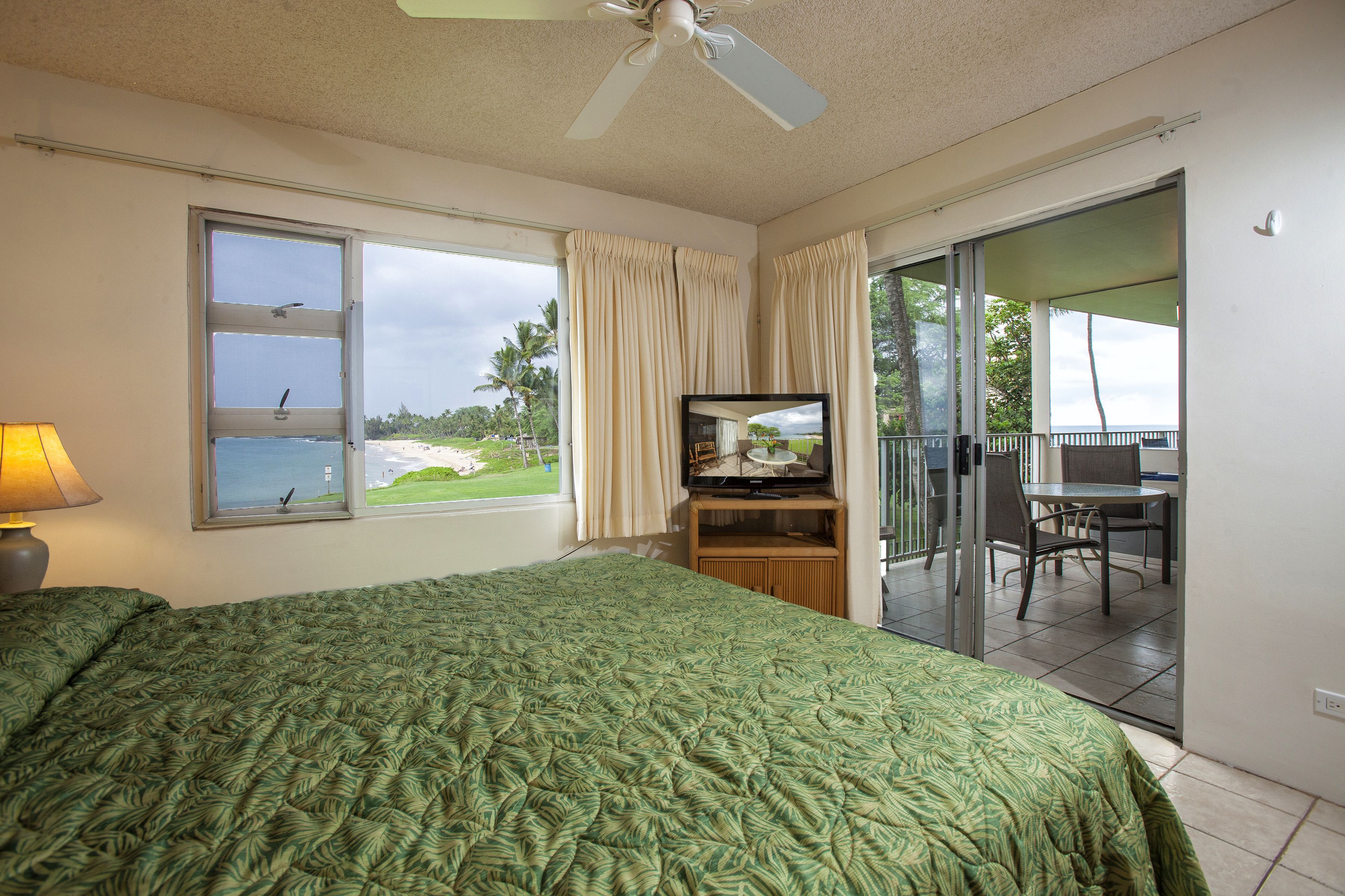 A hotel room with a bed, a TV, a balcony with a table and chairs, and a view of the beach.
