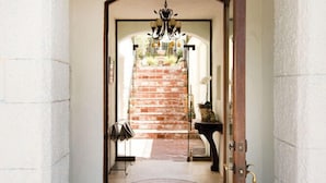 A hallway with a white wall, a wooden door, a brick staircase, and a chandelier.