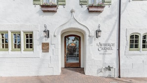 A white building with a wooden door, green window shutters, and a sign reading "LAUBERGE CARMEL HOTEL & RESTAURANT".