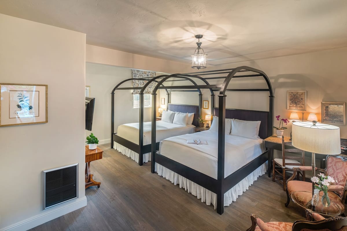 A four-poster bed with a canopy, two bedside tables with lamps, a chair, and a small table with a vase of flowers.