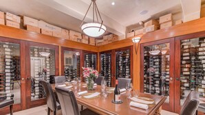 A dining area with a long table set for four, surrounded by wine racks filled with bottles.