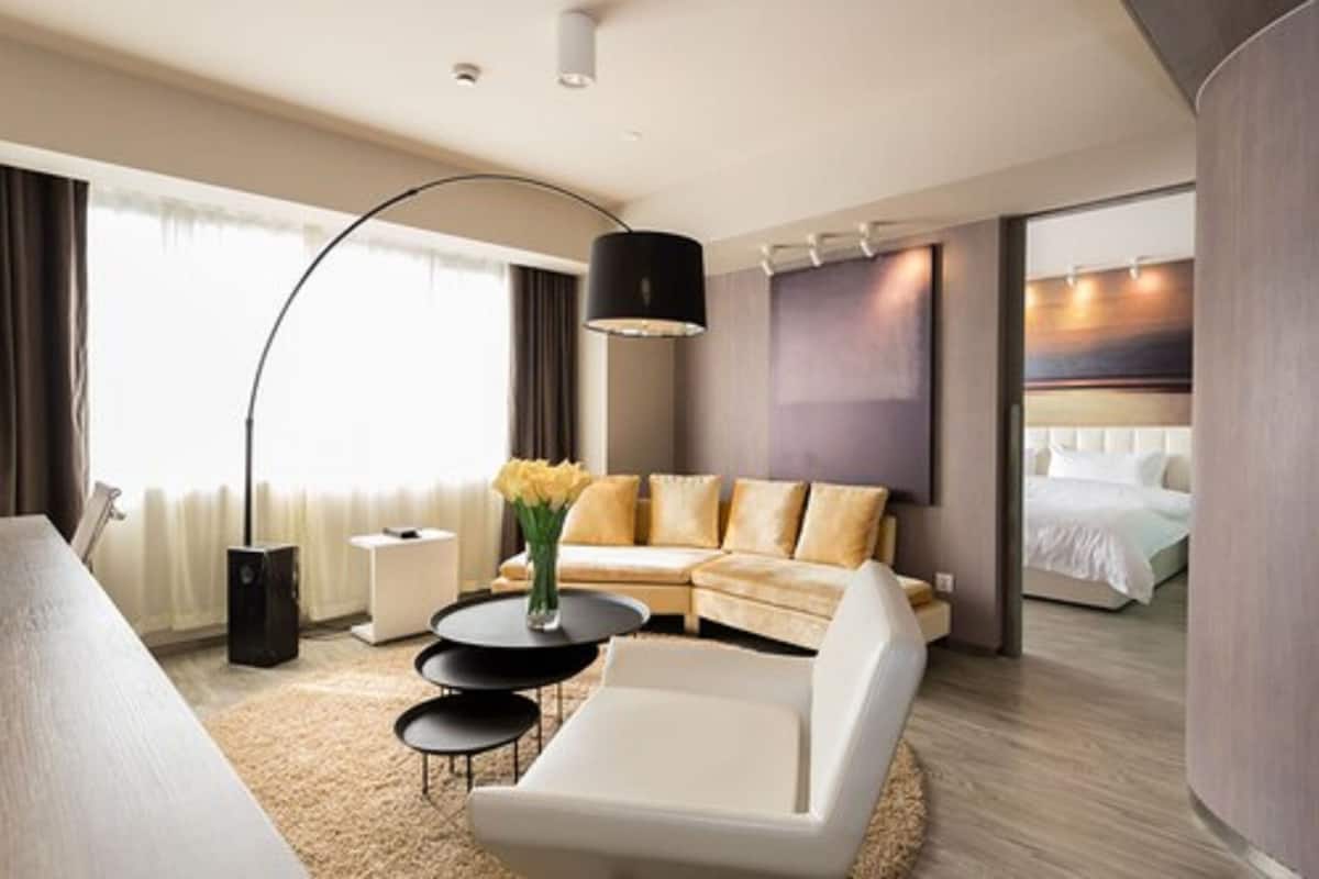 A modern hotel room with a sofa, a white armchair, a coffee table, and a bed.