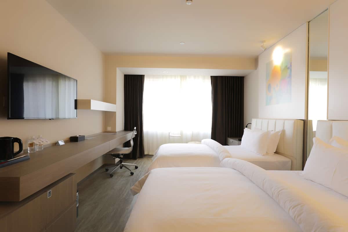 A hotel room with two beds, a desk, a chair, a flat-screen TV, and a large mirror.