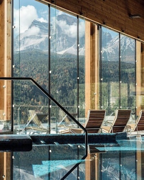 A glass-enclosed swimming pool with lounge chairs, wooden beams, and a mountain view. - Hotel Boite (Borca di Cadore)