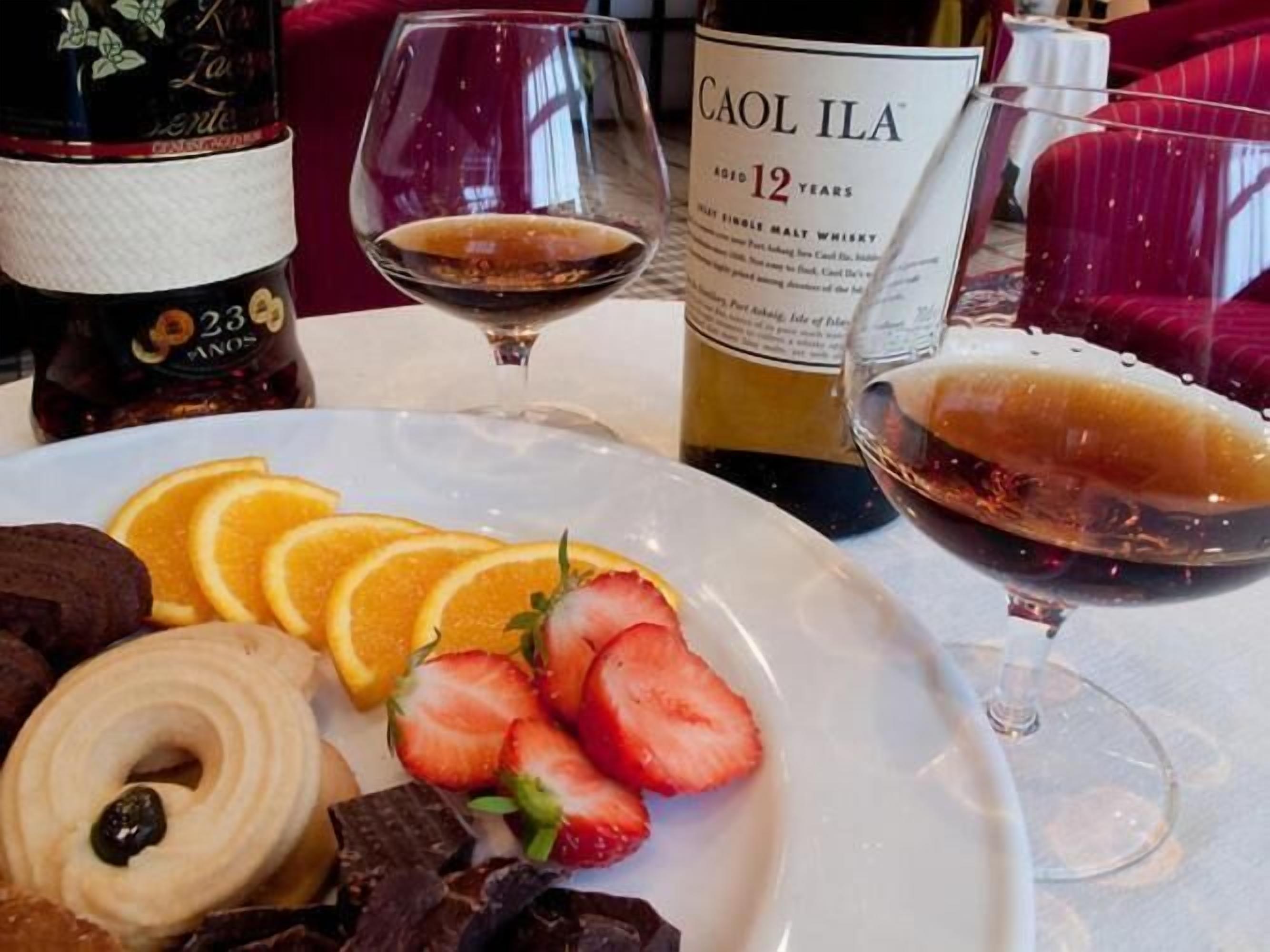 A dining table with a plate of food, a bottle of Caol Ila whisky, and a glass of wine.