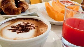 Un desayuno con una taza de café, croissants, melón cantalupo y un vaso de jugo de frutas rojas.
